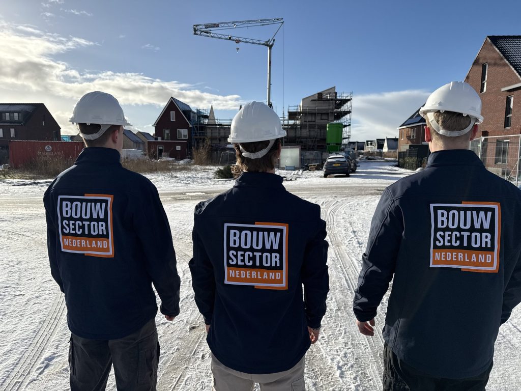 Team van Bouwsector Nederland in donkerblauwe jassen met oranje logo onder een blauwe lucht