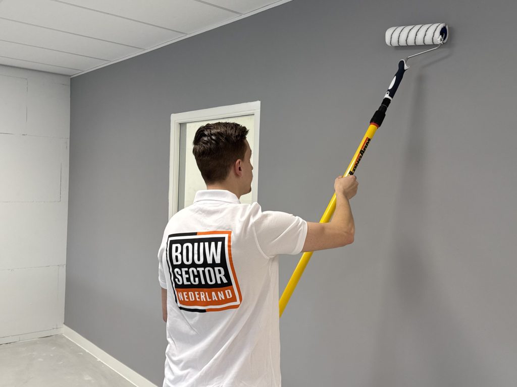 Schilder van Bouwsector Nederland zet een wand in grijze muurverf, links nog een kale muur